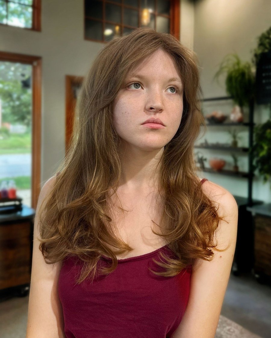 Young woman with long wavy light-brown hair, soft layers and side-swept bangs